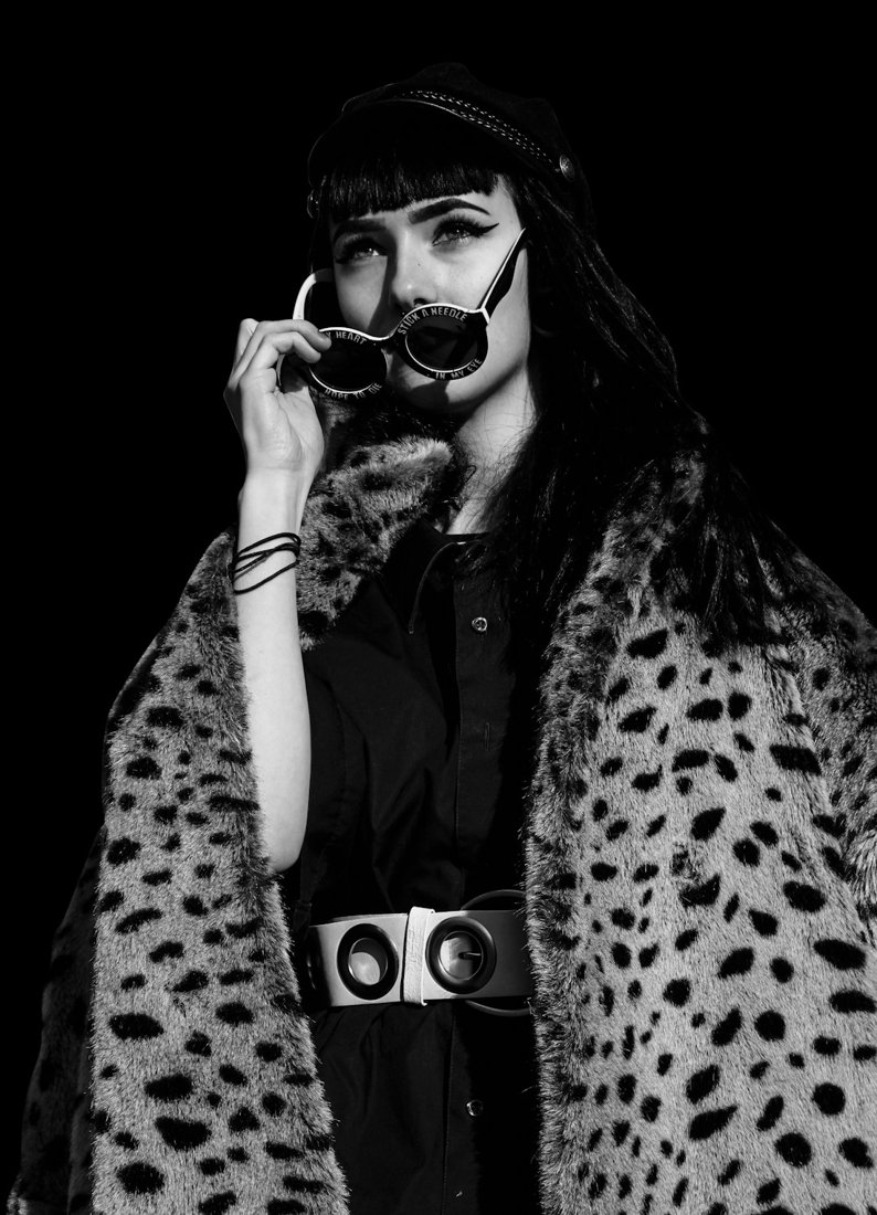 Black-and-white portrait of a woman in a leopard-patterned coat holding sunglasses