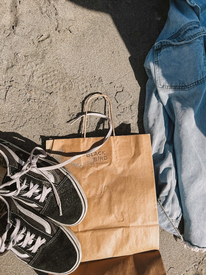 Black canvas sneakers beside a brown paper bag and blue jeans on the ground