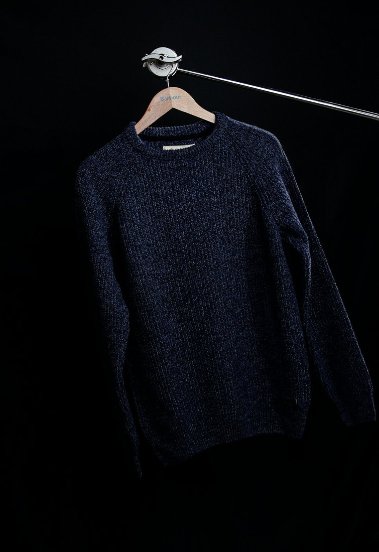A dark knitted sweater on a wooden hanger against a black background