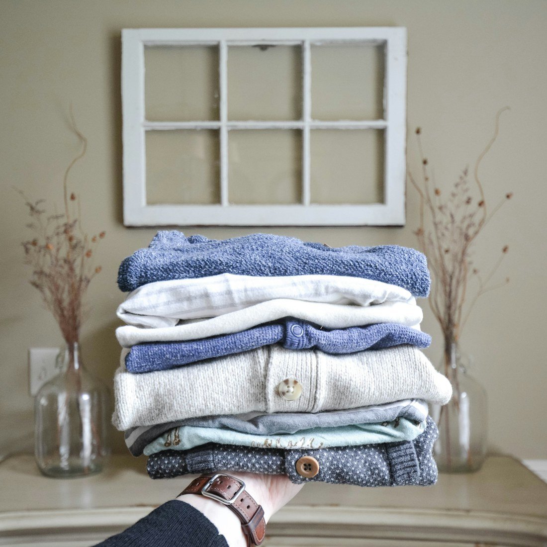 A hand holding a stack of folded blue, white and gray knitwear