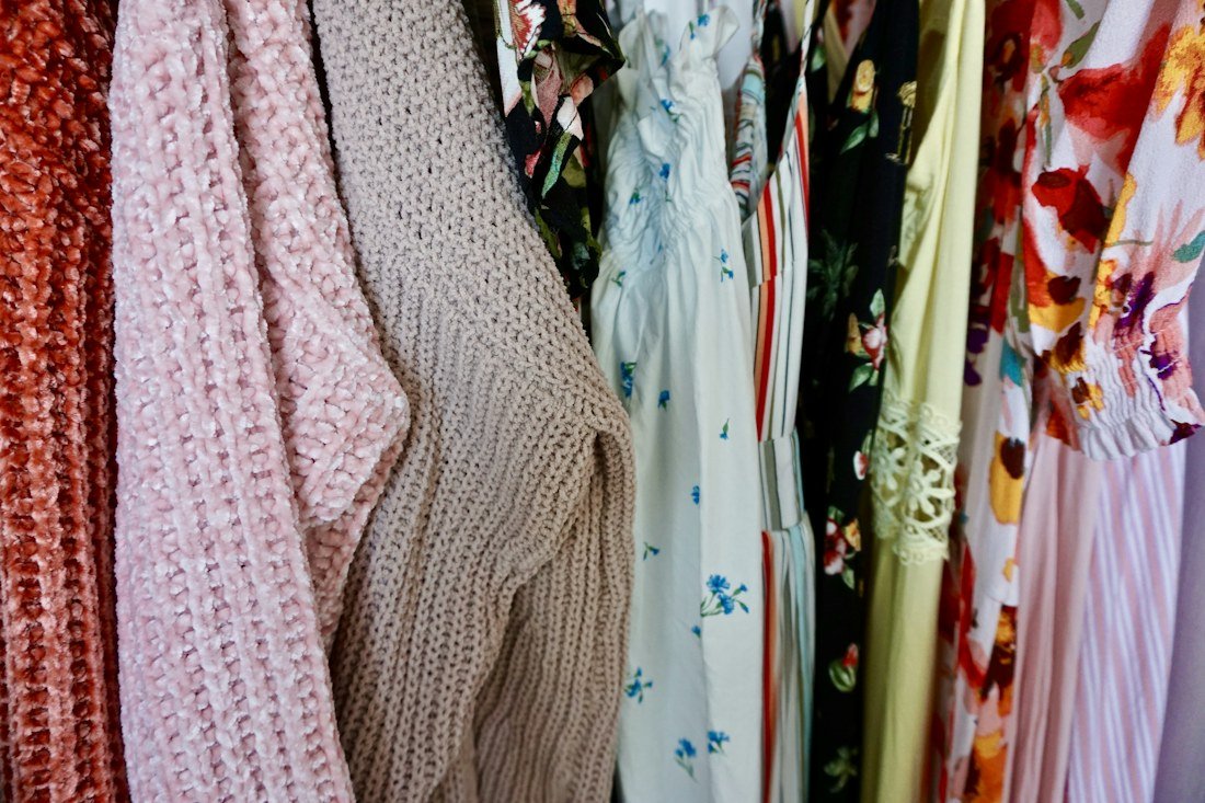 Pink and gray knitwear hanging beside floral dresses in a closet
