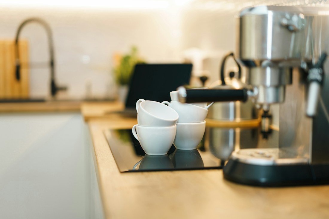 White coffee cups beside a silver espresso machine on a wooden kitchen counter