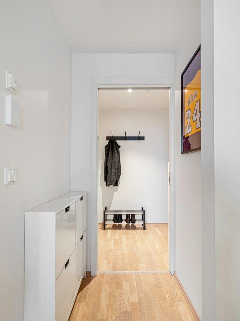 A bright white hallway with a wall-mounted coat rack, a shoe rack and narrow storage cabinet