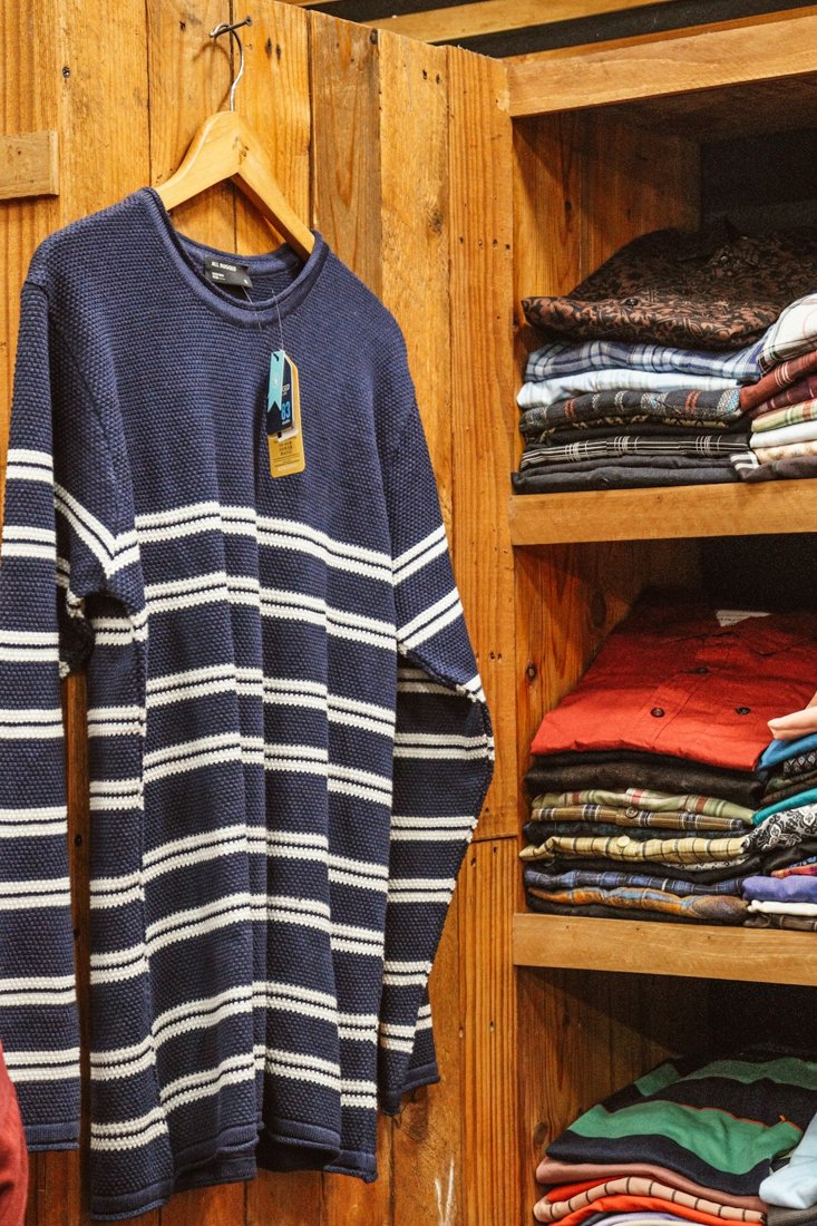 A blue-and-white striped sweater hanging beside shelves of folded shirts in a wooden wardrobe