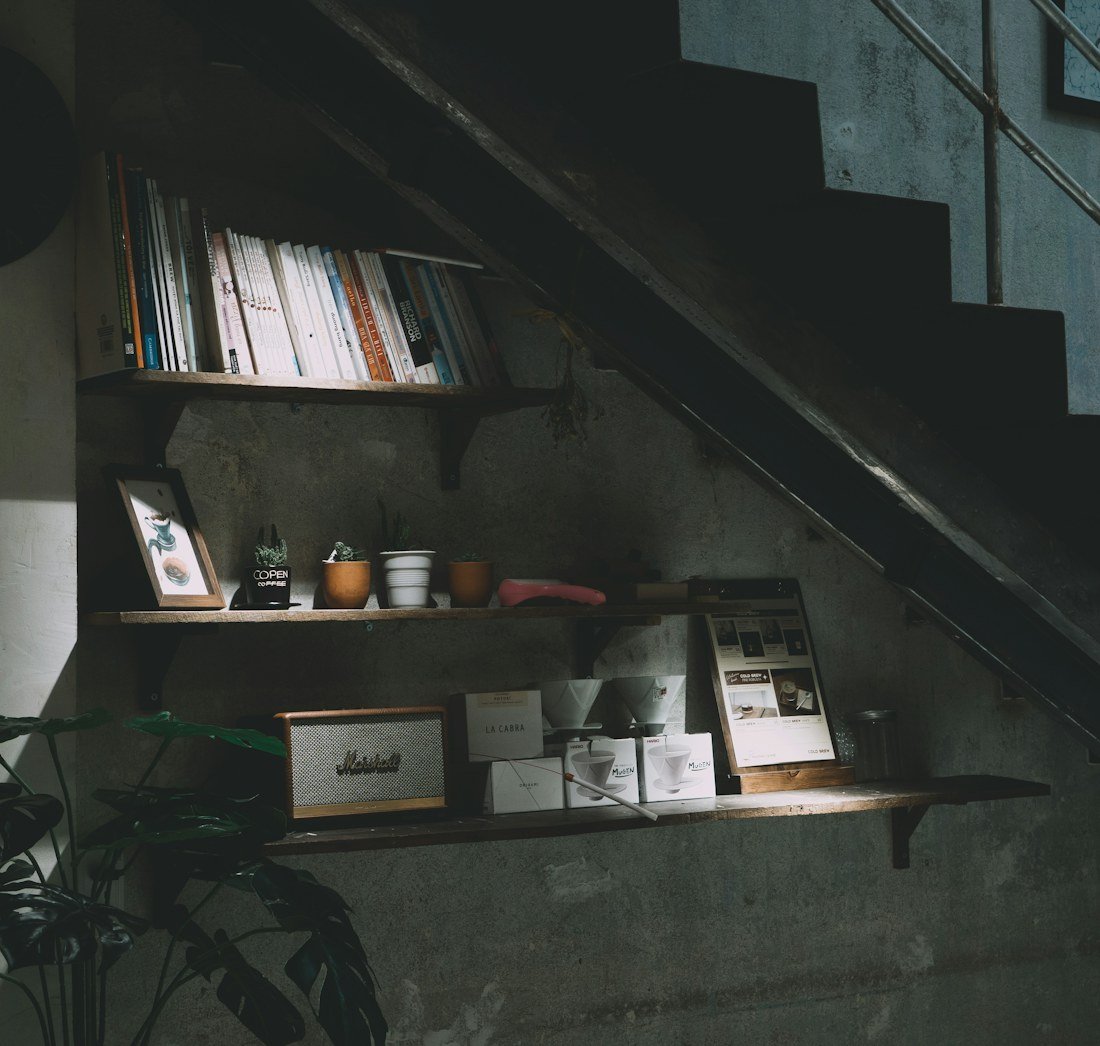 Books, framed pictures and cups on shelves beneath a dark staircase