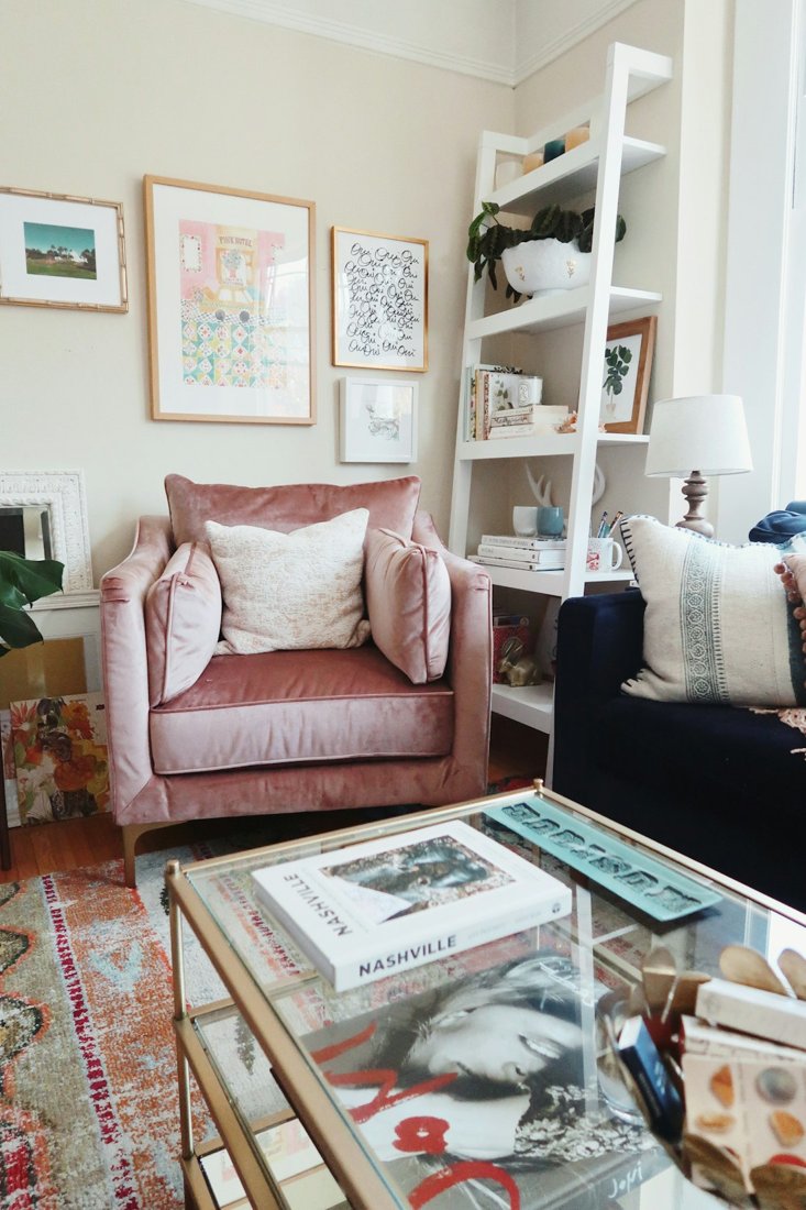 A pink armchair beside a glass coffee table and tall bookshelf in a bright living room