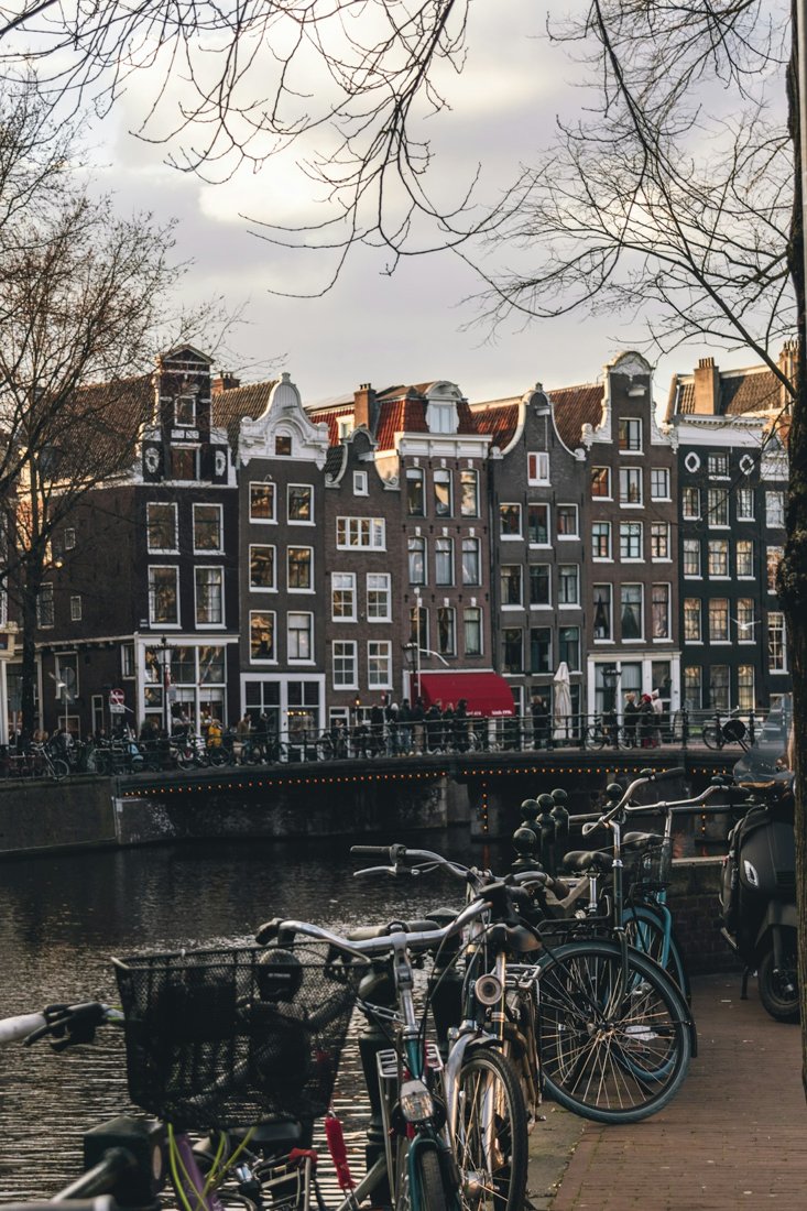 Bicycles beside an Amsterdam canal with narrow brick houses across the water