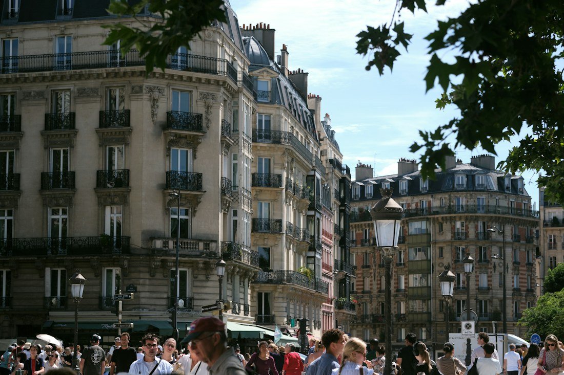 People walking below ornate stone apartment buildings on a Paris street