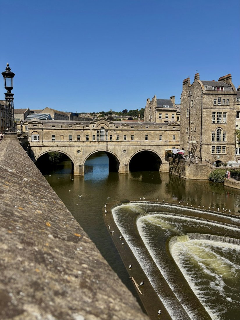 Pulteney Bridge and the curved River Avon weir in Bath beneath a blue sky